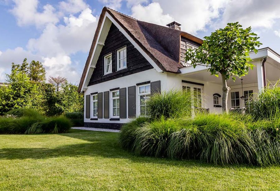 Witte woning met donkere houten gevelbekleding en een rieten kap